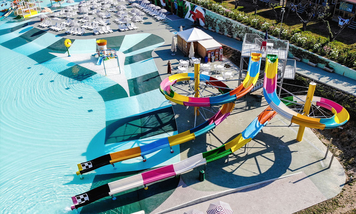Colorful water slides winding into a large swimming pool, surrounded by loungers and umbrellas in a waterpark setting at Cisano/San Vito