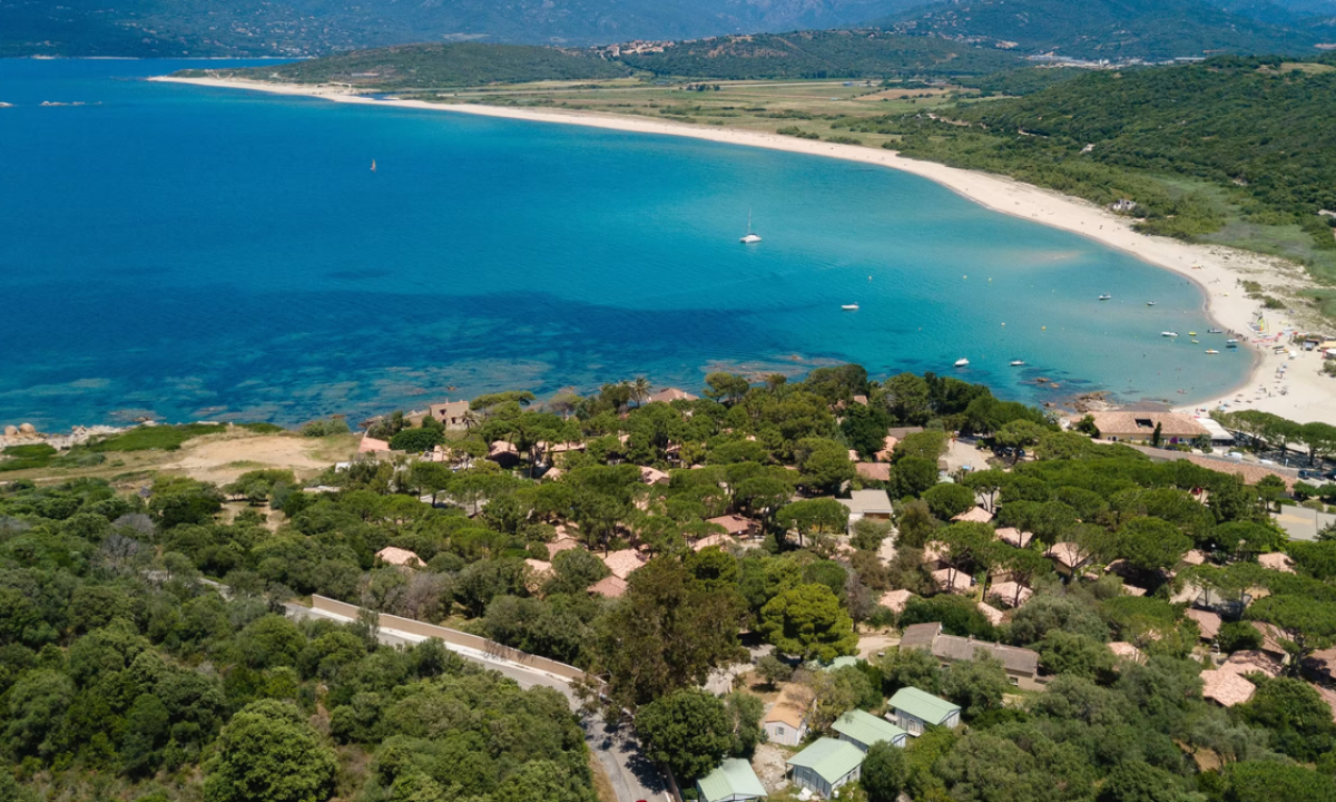 Aerial view of houses amidst lush trees near a curving sandy beach and vibrant blue sea at U Livanti