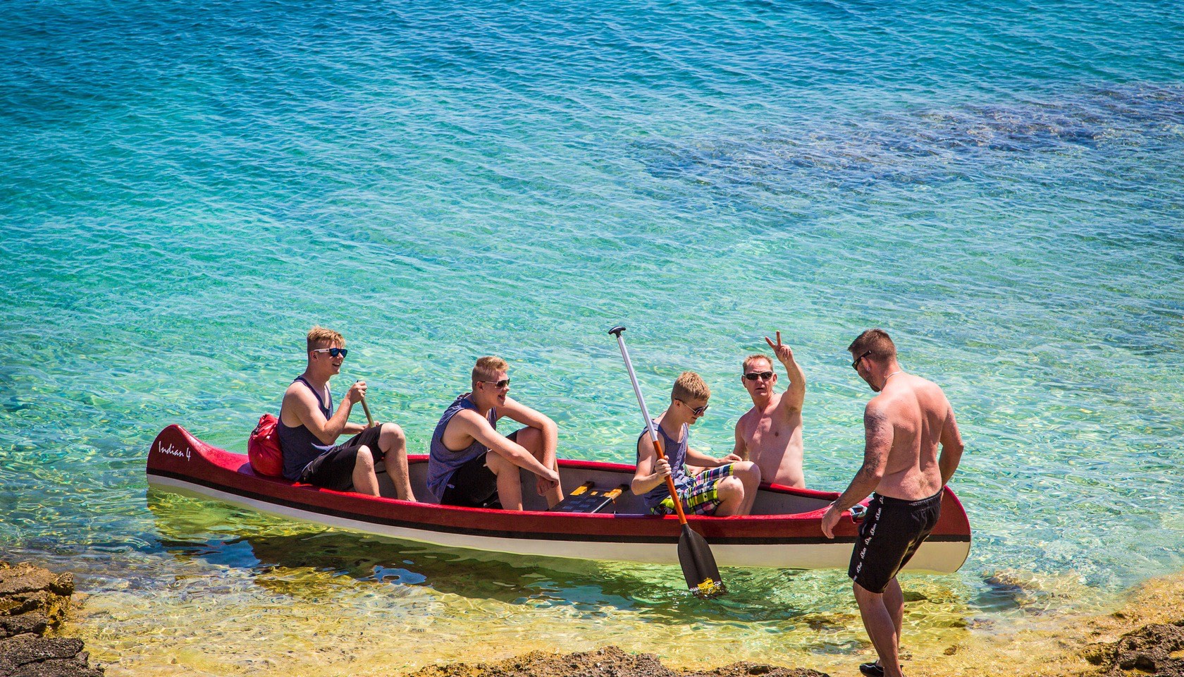 A group of people canoeing in shallow, clear water by a rocky shore at Stupice