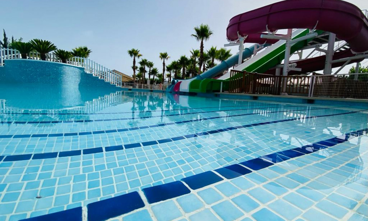 View of a bright pool with slides, surrounded by palm trees and clear skies at Lo Monte