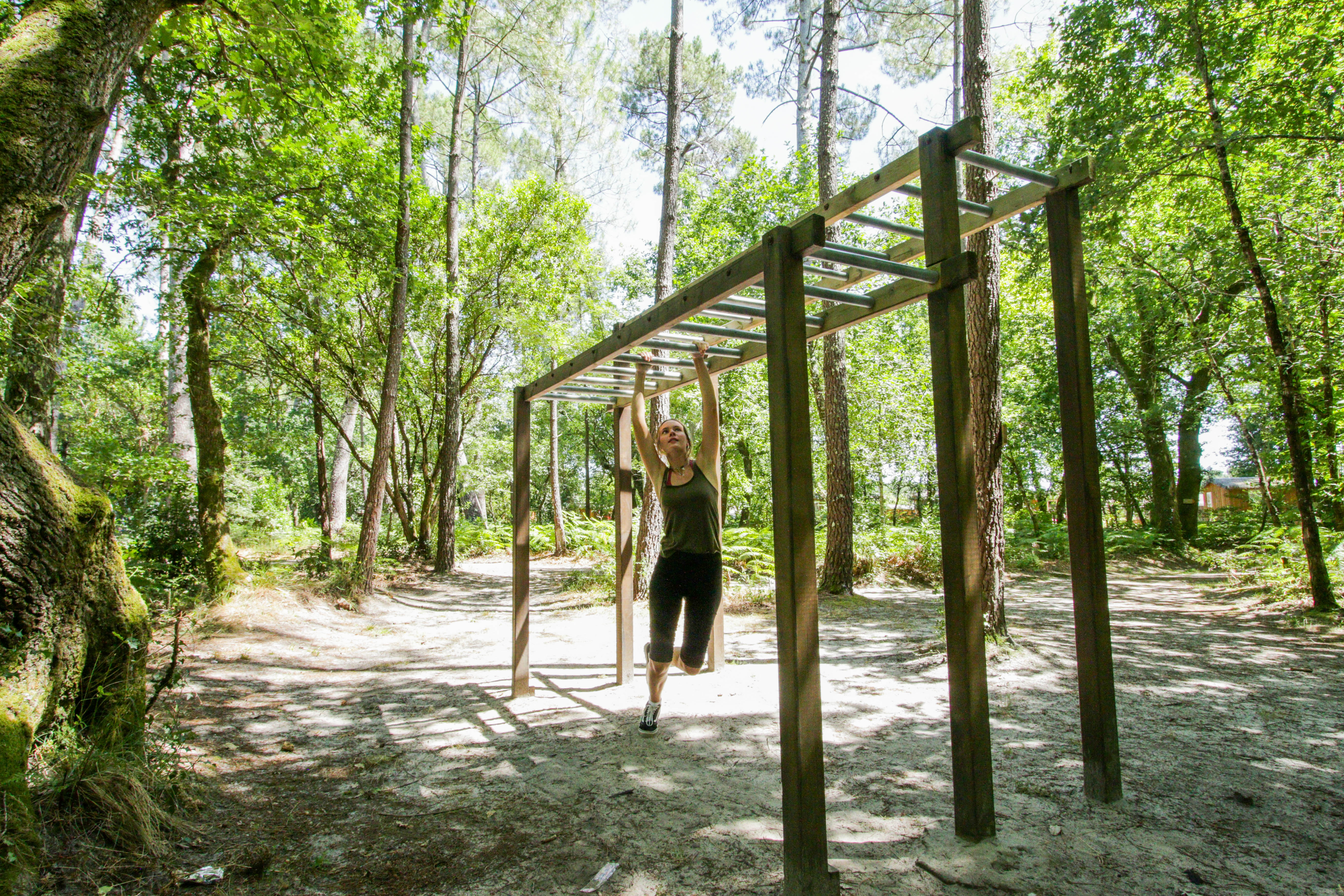 Person swinging on monkey bars in a wooded area at Au Lac de Biscarrosse
