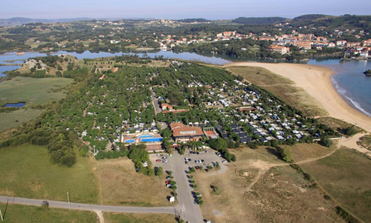 Aerial view of a campsite with pools and parked cars near a sandy beach and distant residential area at Playa Joyel