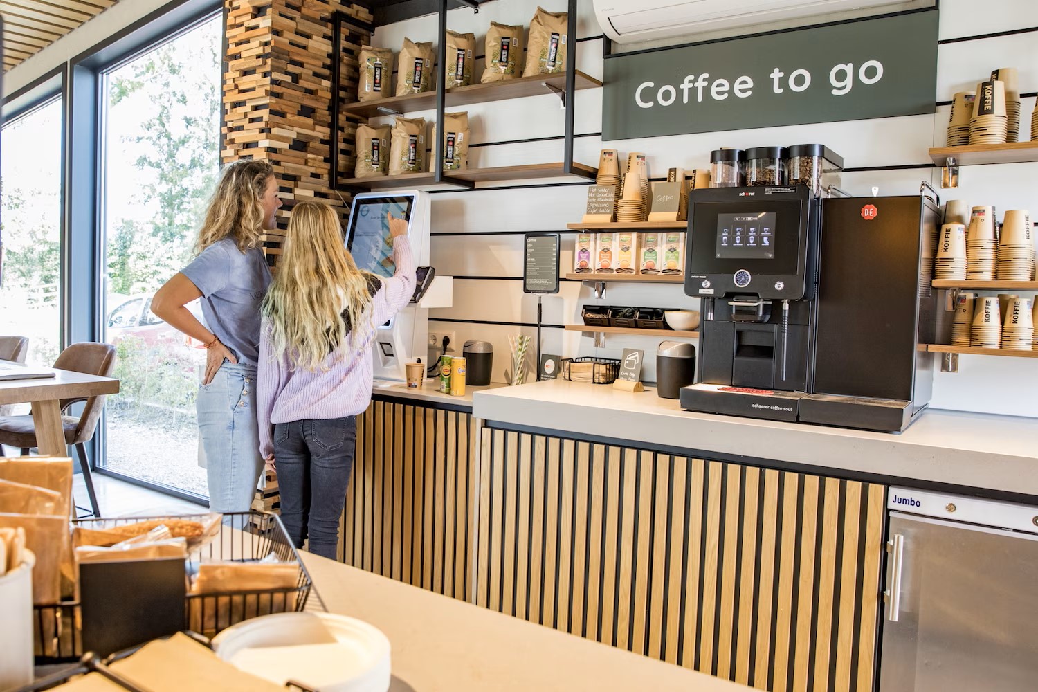 Two people ordering coffee at an automated kiosk in a modern, well-lit coffee shop at Park Wijdenes
