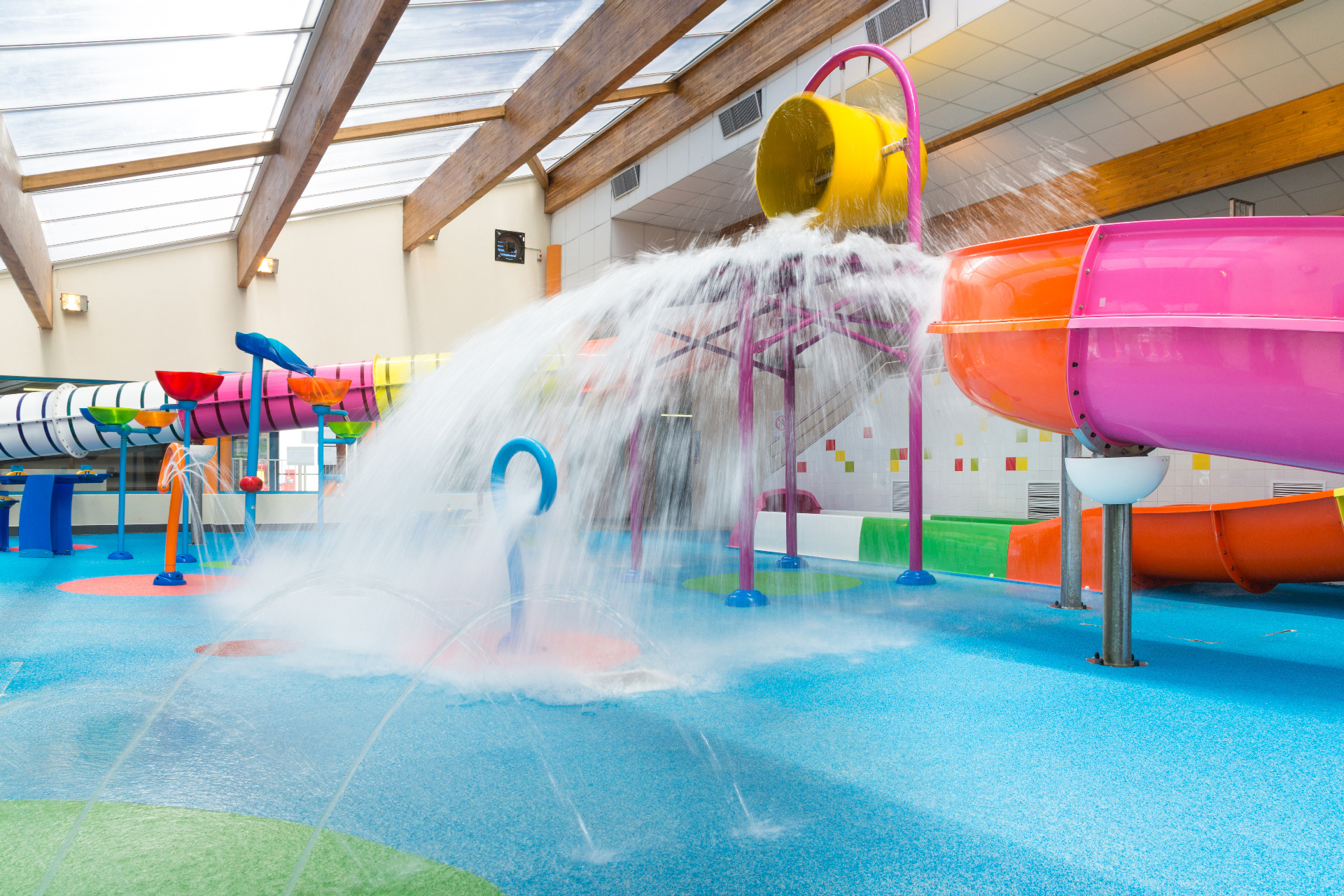 Water bucket dumping water inside colorful indoor water park with slides and play structures at Le Littoral