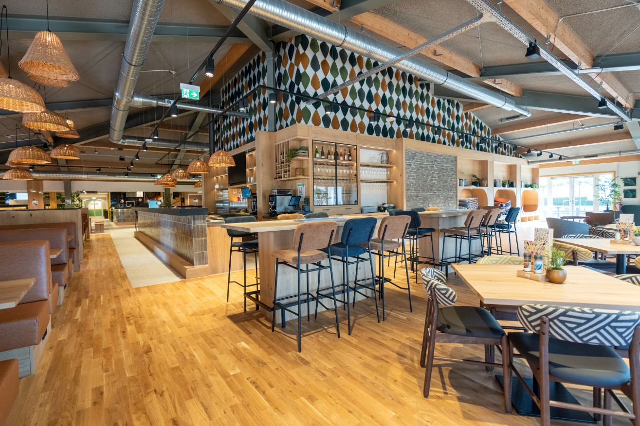 Modern dining area with wooden tables and chairs, featuring hanging lights and colorful wall patterns at Ferienresort Cochem