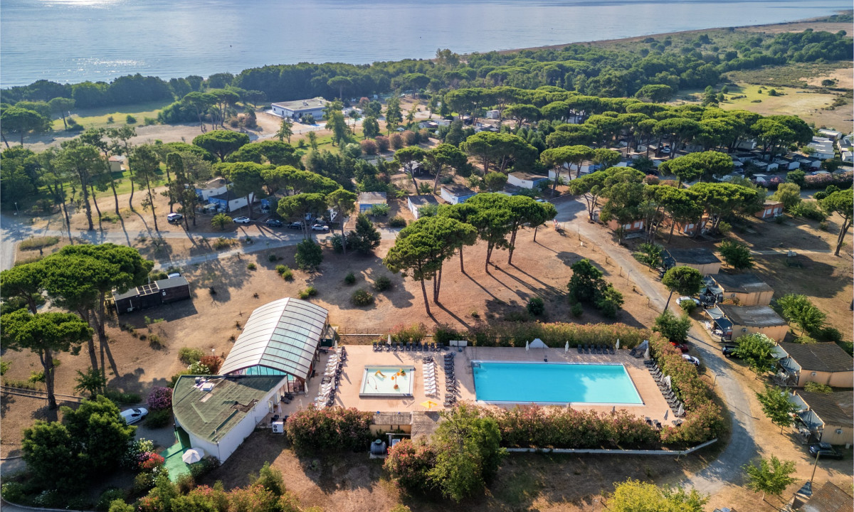 Aerial view of a campsite featuring a swimming pool and scattered trees, near a scenic coastline at Le Domaine d'Anghione