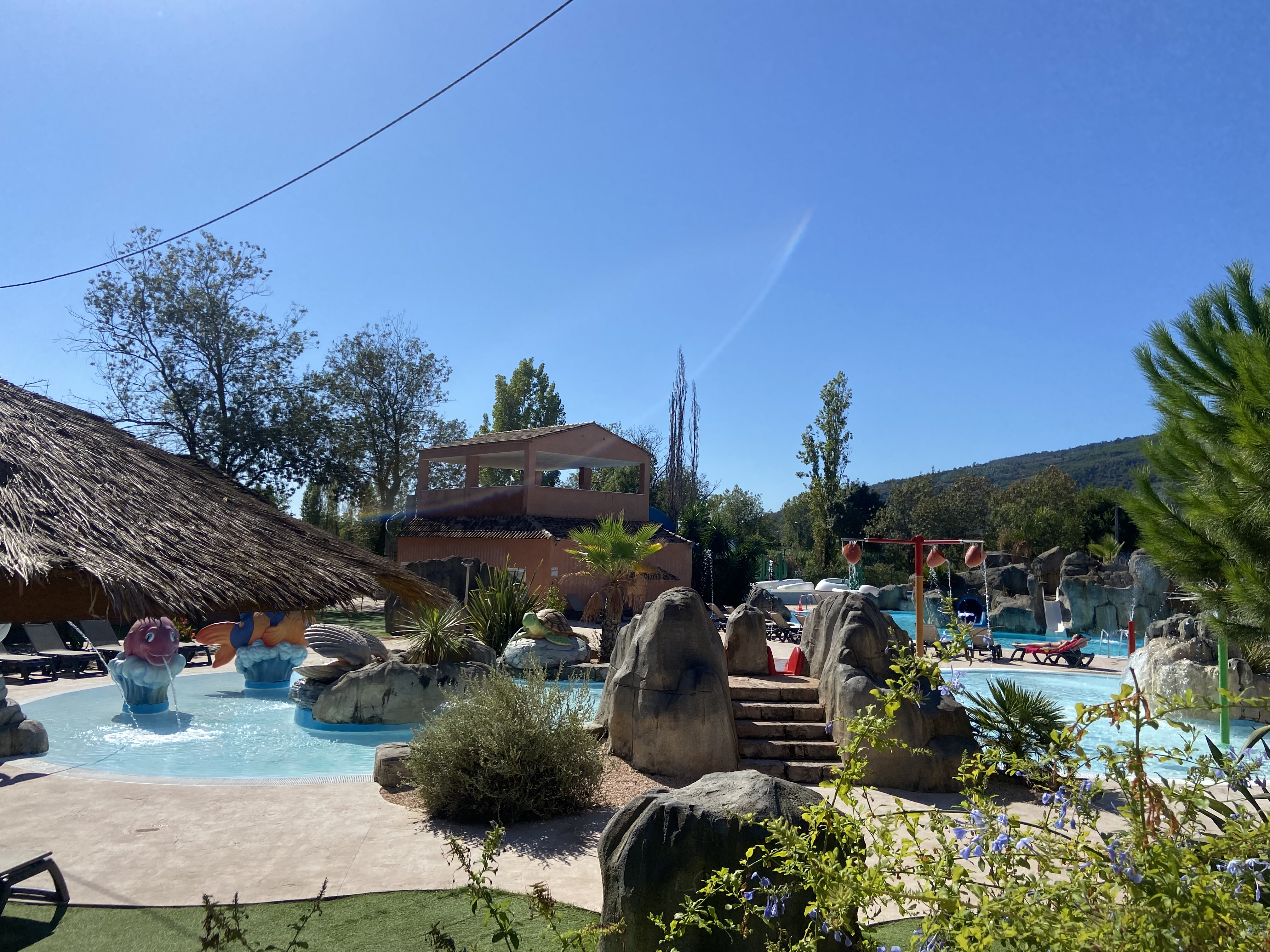 Water park with slides, animal sculptures in small pool, and deck chairs under umbrellas, surrounded by trees at Le Saint Louis