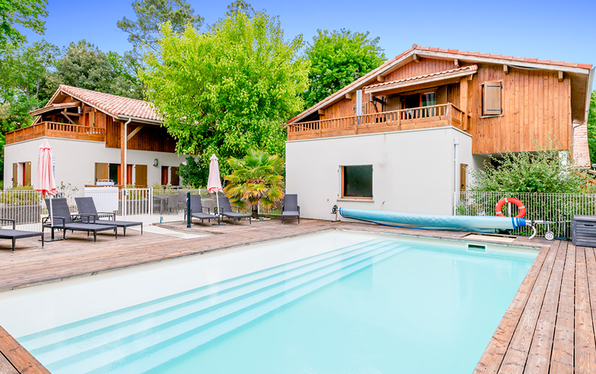 House with a pool, wooden deck, lounge chairs, and trees in the background at Residence Les Rives du Lac