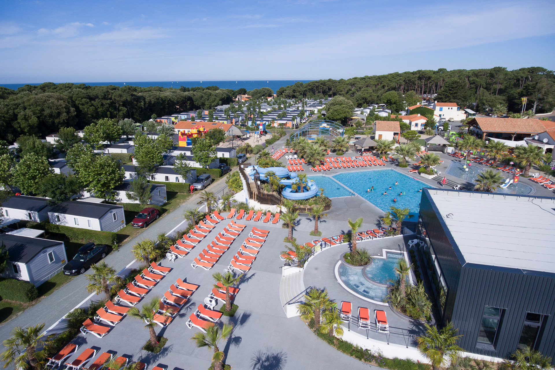 Swimming pool with sun loungers, surrounded by mobile homes, trees, and a forested coastline in the distance at Le Littoral