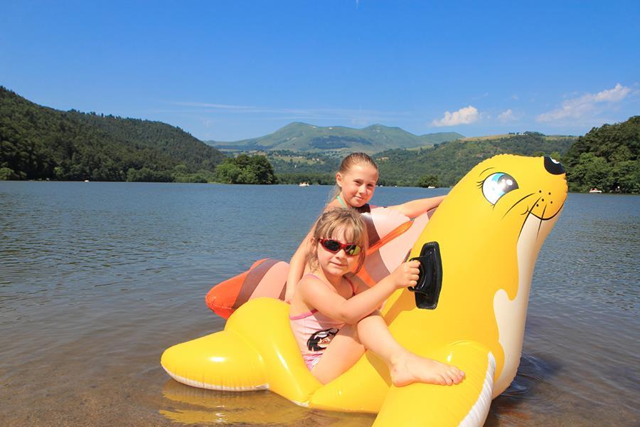 Two children on an inflatable seal in a lake with mountains and trees in the background at Paradis l'Europe