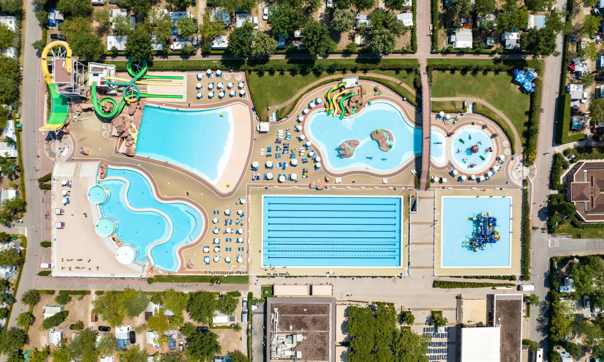 Aerial view of a large recreational pool complex with slides and sunbathing areas surrounded by greenery at Marina di Venezia