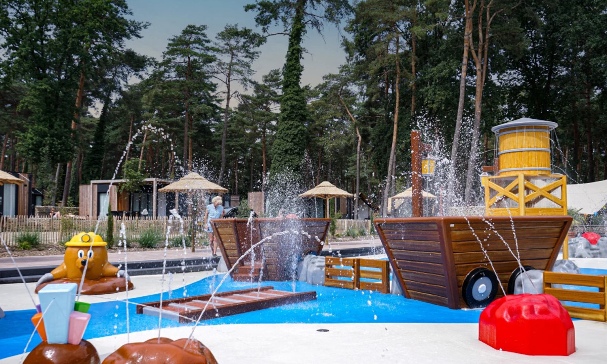 Splashing water features in a colorful, playful water park surrounded by cabins and tall trees at Europarcs Hoge Kempen