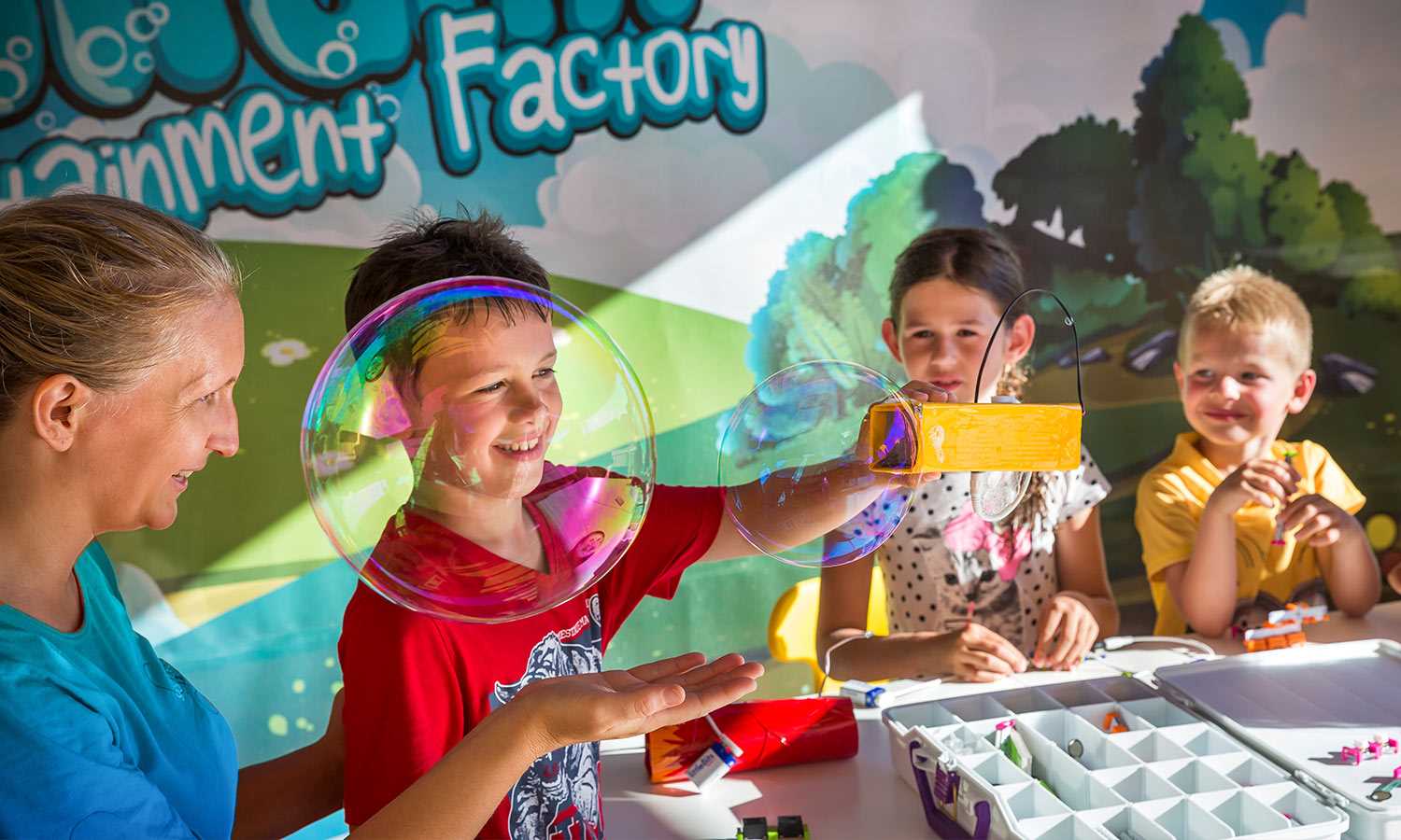 Children create colorful bubbles indoors, assisted by an adult, surrounded by playful, painted walls at Aminess Avalona Camping Resort