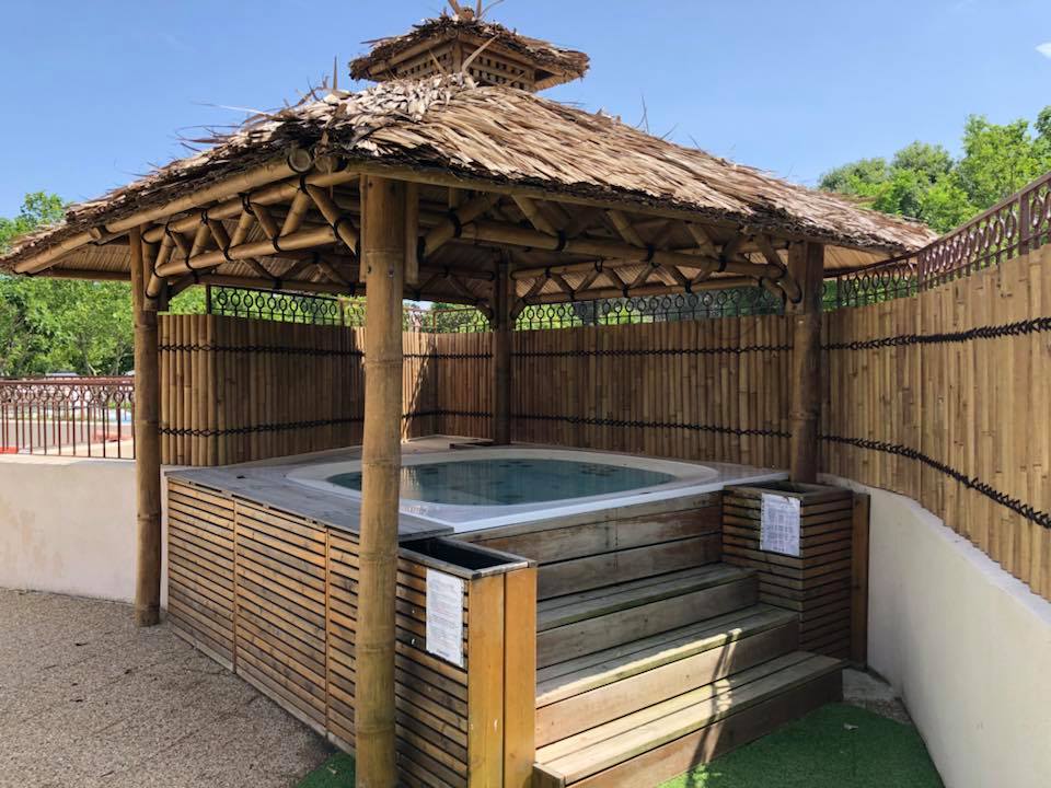 Hot tub under bamboo pergola, surrounded by wooden fence and greenery at Parc Mogador