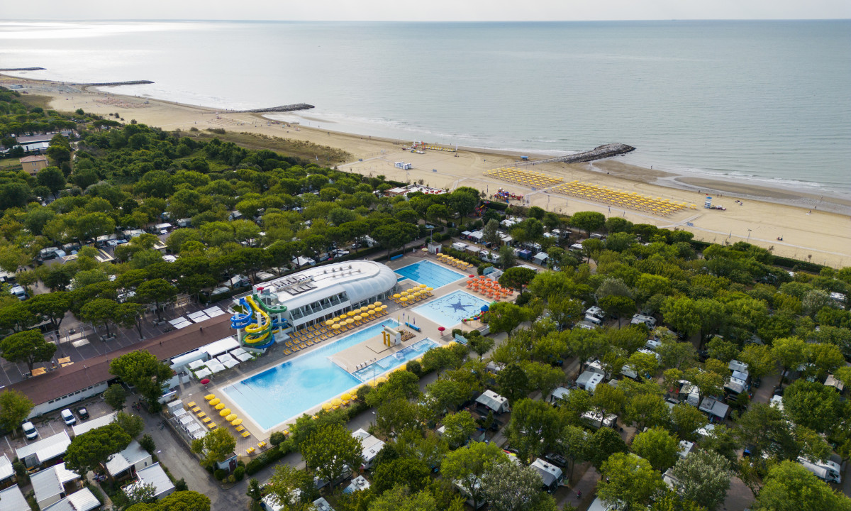 Aerial view of colorful water slides beside a pool, surrounded by trees and adjacent to a sandy beach at Garden Paradiso