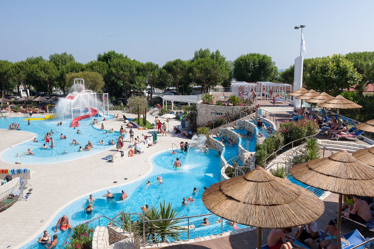 People swimming and relaxing in a large pool with slides and surrounding greenery at Ca'Pasquali