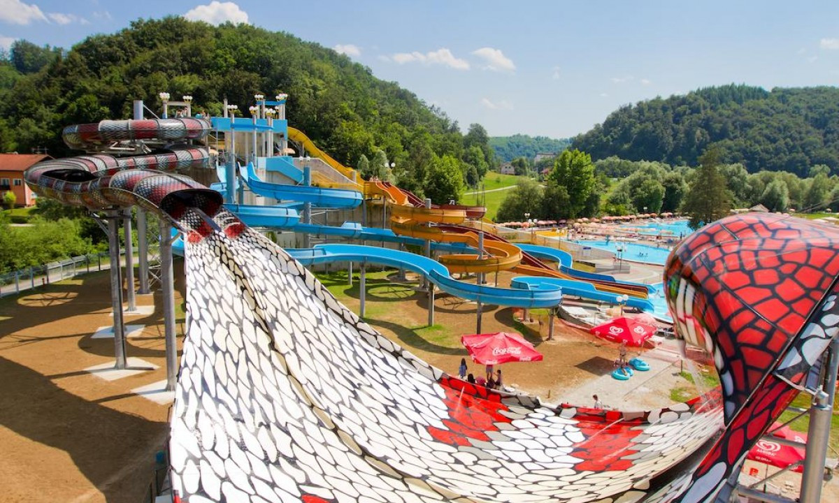 Colorful water slides intertwine and descend, surrounded by lush greenery and recreational areas at Village Lipa