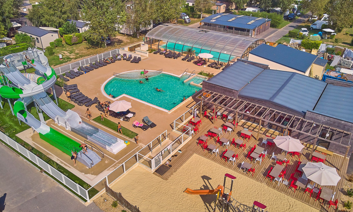 Waterslides descend into a pool, with people swimming and relaxing; nearby, a deck hosts tables and chairs at Marvilla Parks Riva Bella