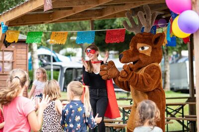 Mascot in a reindeer costume and a woman in a cape entertaining children under a decorated wooden shelter at Petite Suisse