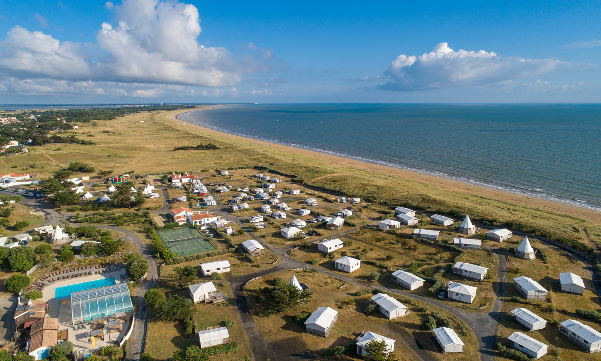 Campsite with various tents and cabins overlooking a vast, sandy beach and calm ocean under a blue sky at Le Midi