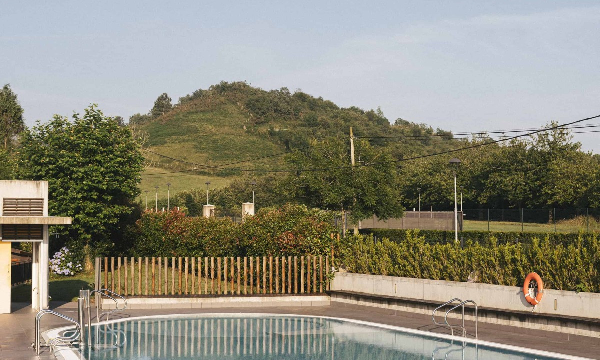 Swimming pool reflecting clear sky, surrounded by greenery and hills, with modern fencing and planters at Wecamp San Sebastián