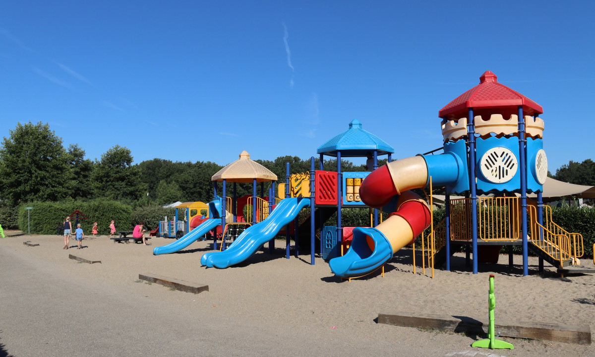 Children's colorful playset with slides and tubes in a sandy playground area, surrounded by greenery and people at Recreatiepark Duinhoeve
