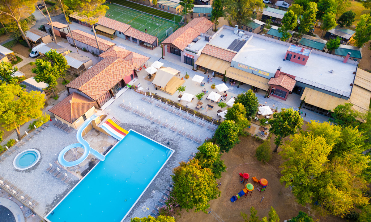Swimming pool with colorful slides adjacent to a large patio filled with loungers; surrounding buildings and trees at Trasimeno Glamping Resort