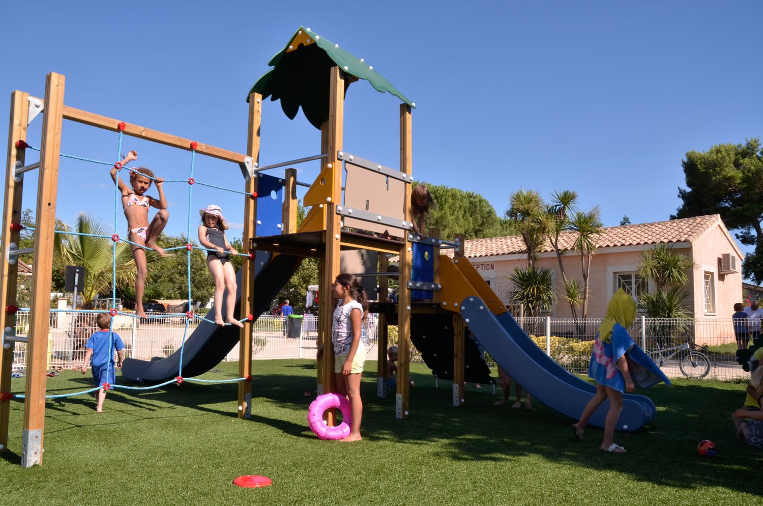 Children playing on a colorful playground with slides and climbing equipment, surrounded by grassy area and buildings at Bon Port