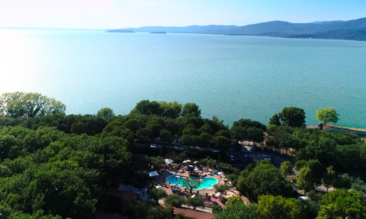 A swimming pool surrounded by trees beside a large, calm lake and distant mountains at Cerquestra