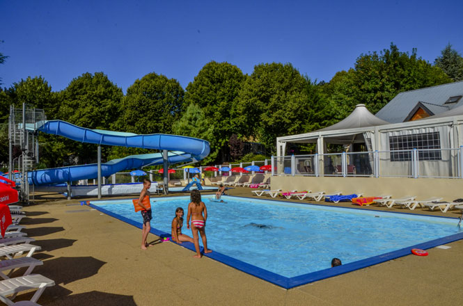 Children swim and play in a pool with a blue slide, surrounded by loungers and trees at Paradis l'Europe