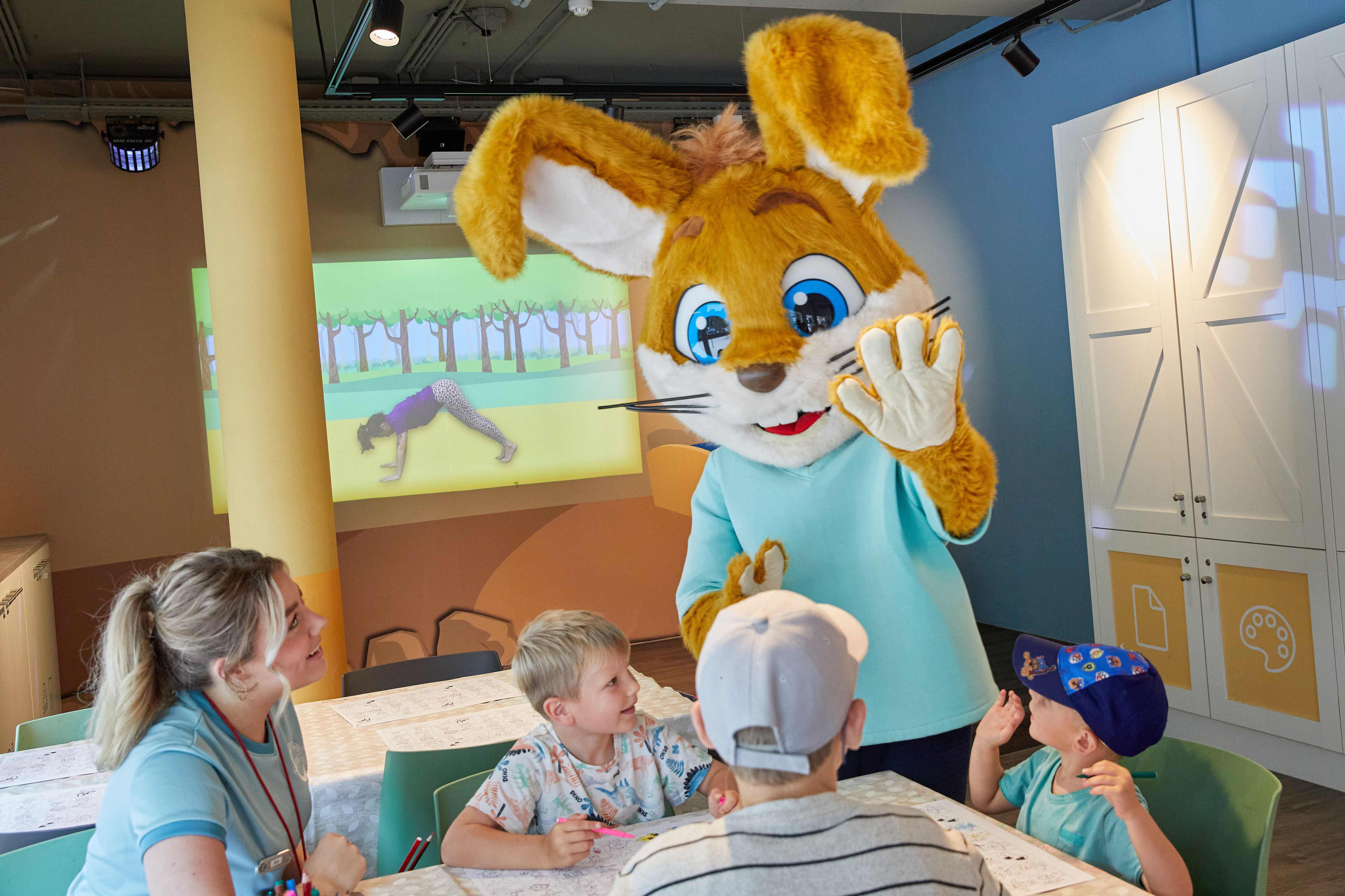 A person in a rabbit costume entertains children and staff who are seated around a table in a brightly lit room at Kijkduinpark