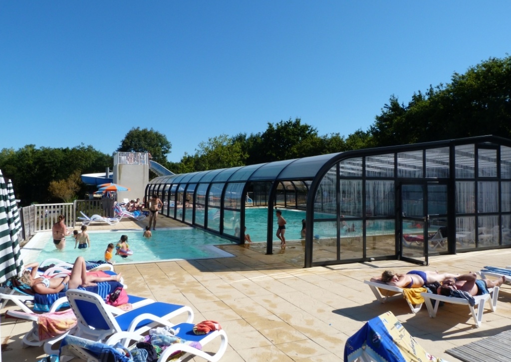 People relaxing and swimming in a pool area, with lounge chairs and a transparent pool canopy at Domaine de Bréhadour