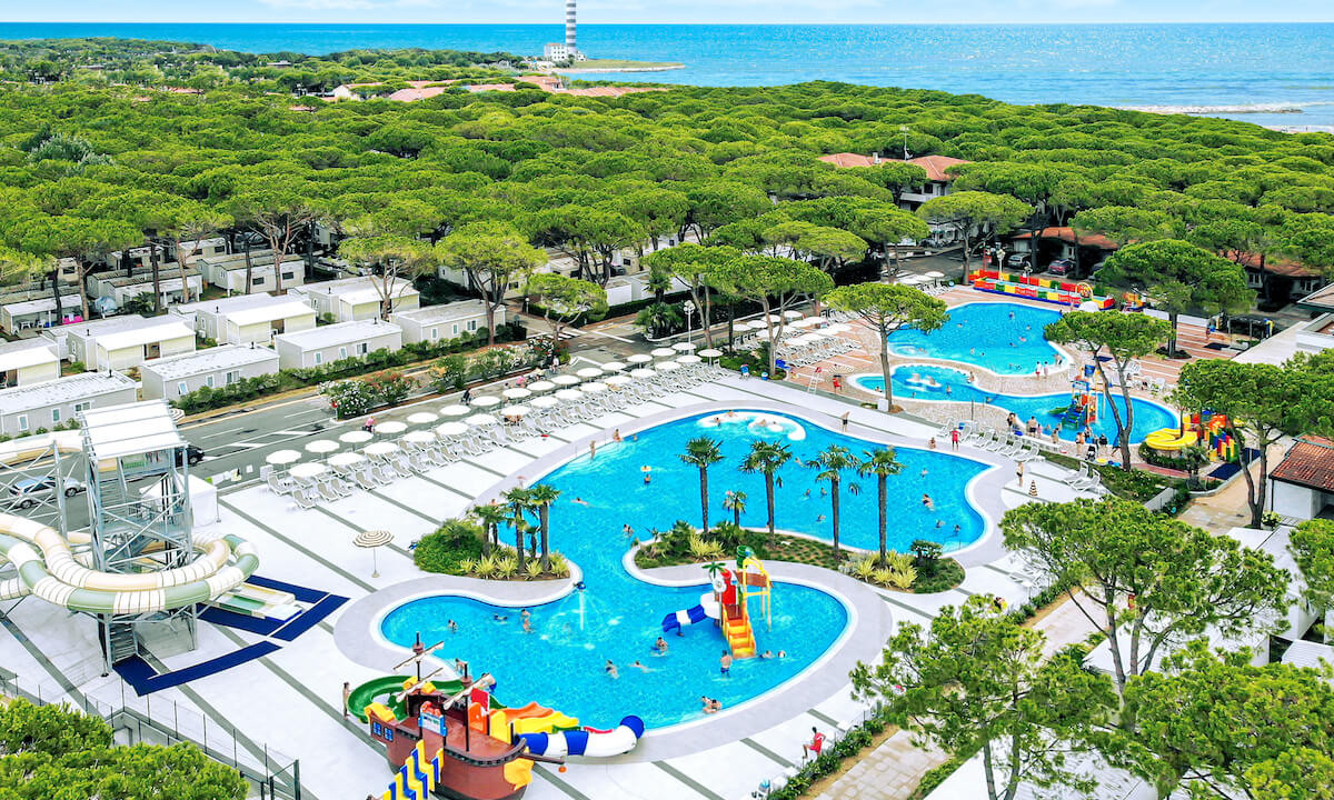 Bright blue swimming pools with slides and sunbathers, set amid lush green trees near the coastline at Residence Village