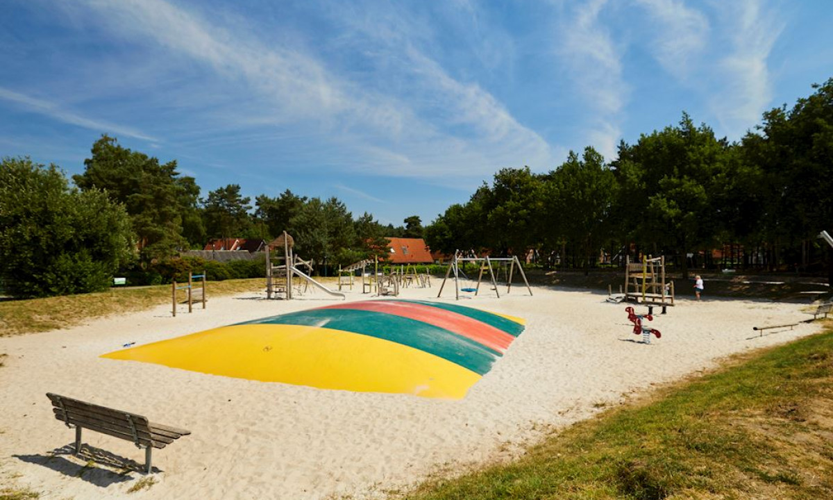 Children's playground with a multicolored bouncing cushion, surrounded by trees and play structures at Landal Dwergter Sand
