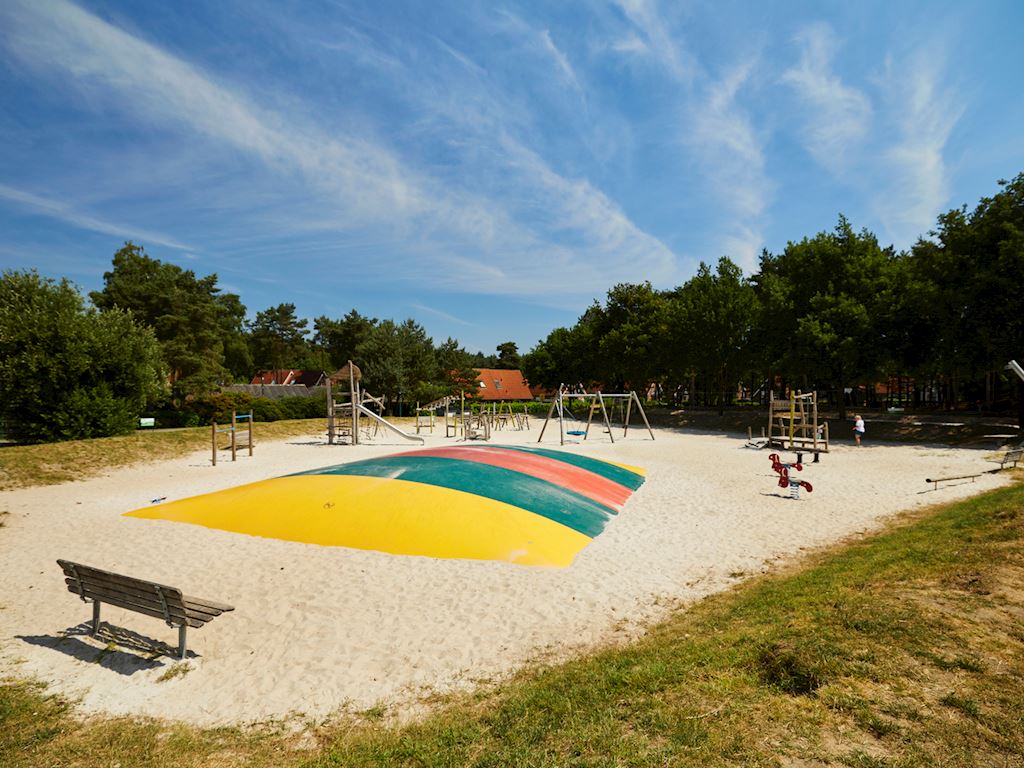 Children's playground with a multicolored bouncing cushion, surrounded by trees and play structures at Landal Dwergter Sand