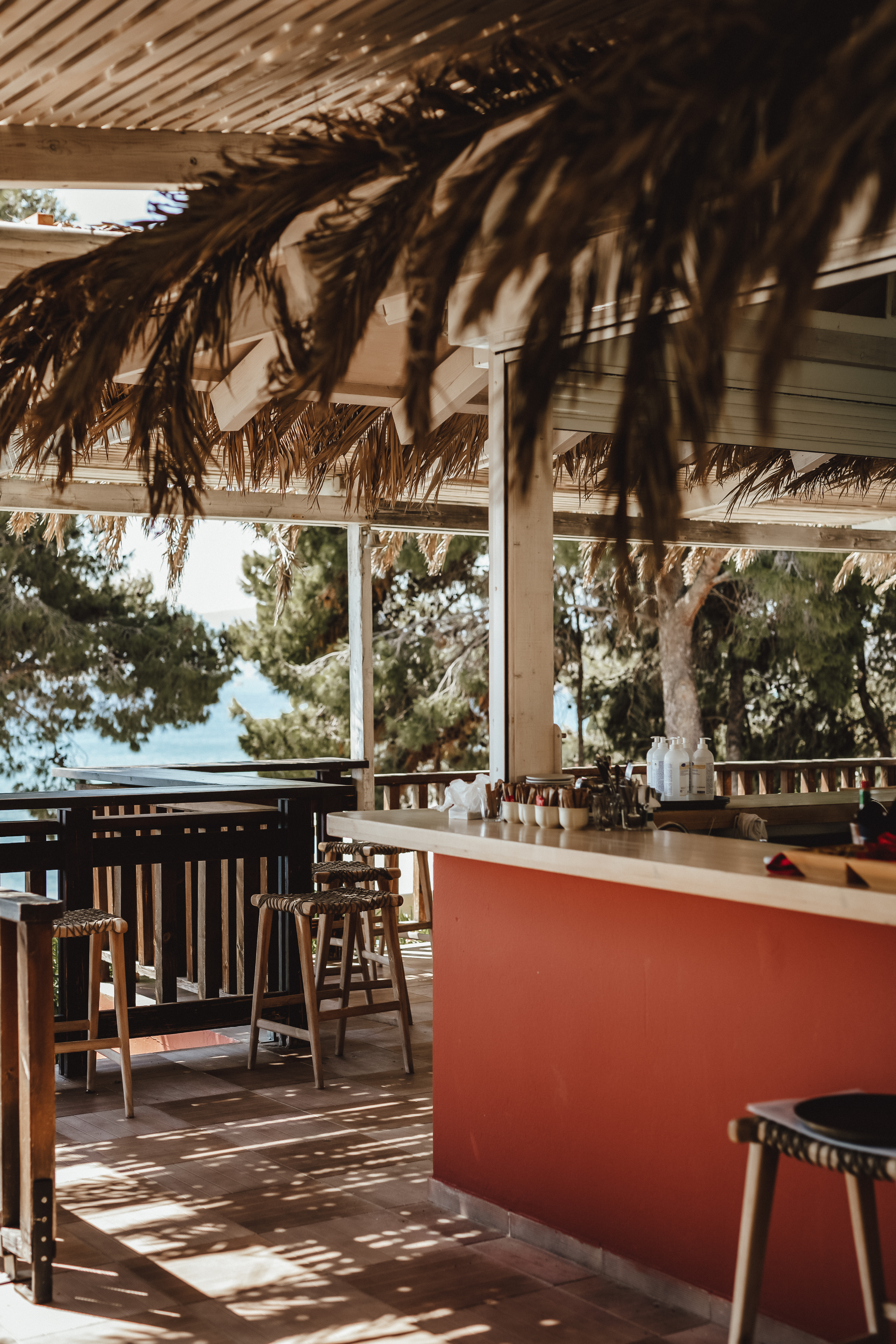 Bar counter with stools under a thatched roof, overlooking trees and a body of water at Candia Park Village