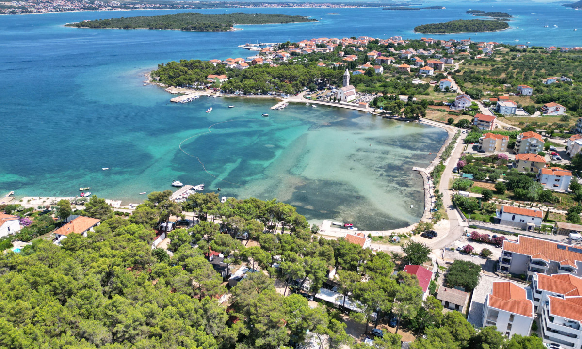 Aerial view of a coastal town with boats docked in clear blue water and houses surrounded by greenery at Camping Taber Pašman