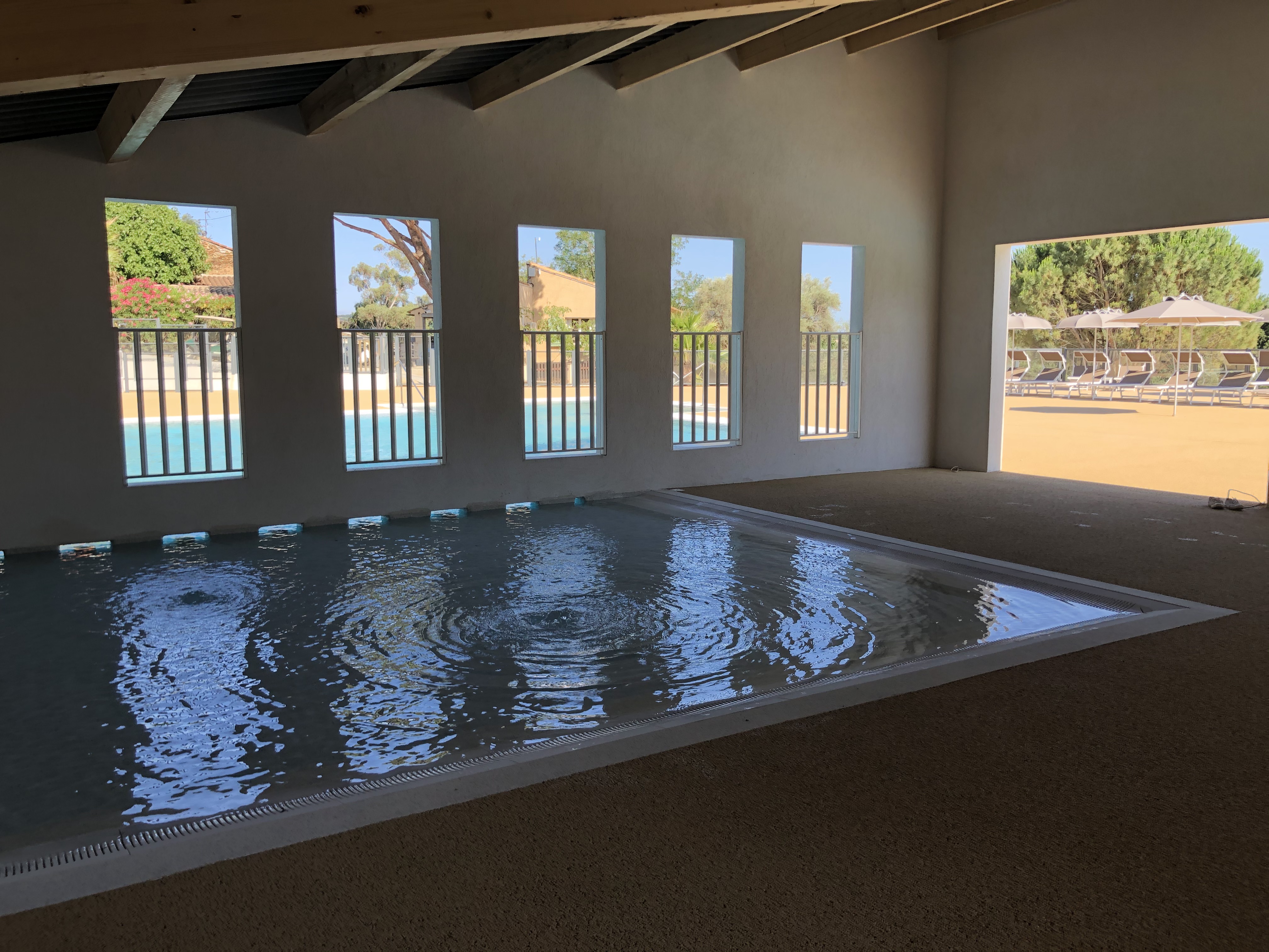 An indoor swimming pool area with windows overlooking an outdoor pool and lounge chairs at Domaine de Miremer