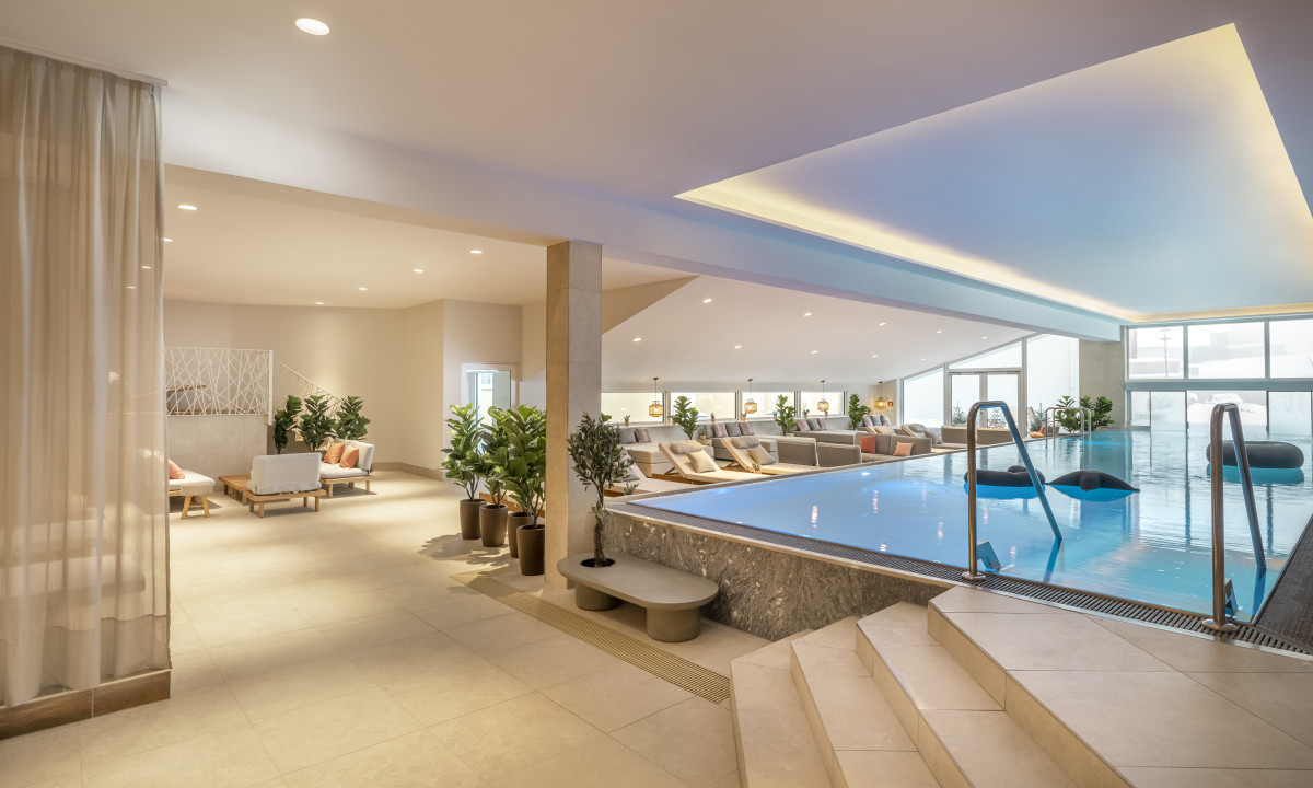 Luxurious indoor pool surrounded by lounge chairs and greenery, under soft lighting in a spacious, modern setting at Valamar Obertauern Hotel