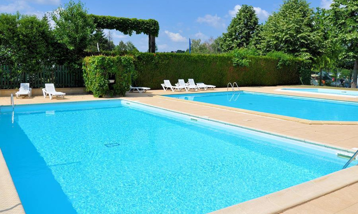 Swimming pool surrounded by sunbeds and greenery with clear blue sky at Le Ranch des Volcans