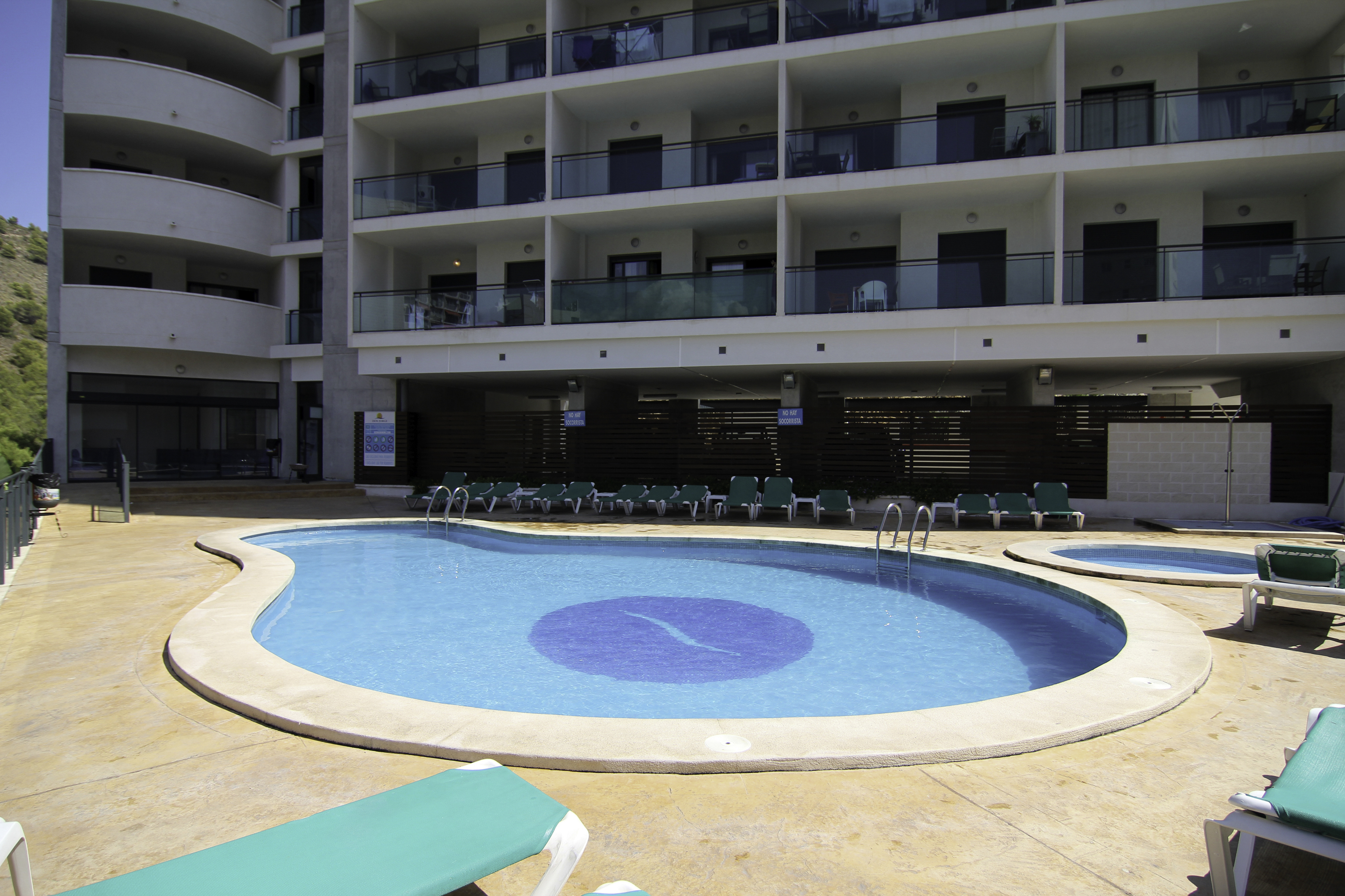 A blue swimming pool with lounge chairs sits in front of a multi-story building at Benidorm Horizon