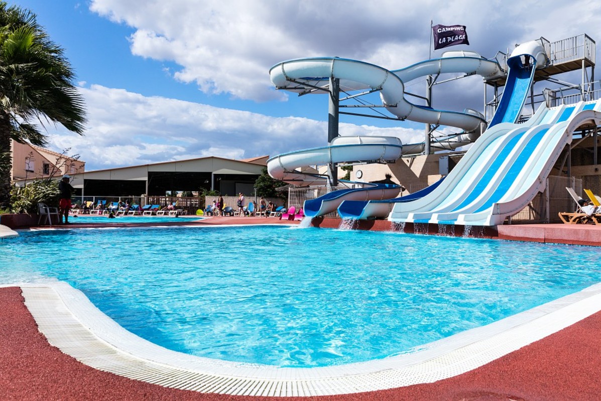 Waterslides spiral into a pool surrounded by people lounging on chairs under a partly cloudy sky at La Plage et le Bord de mer