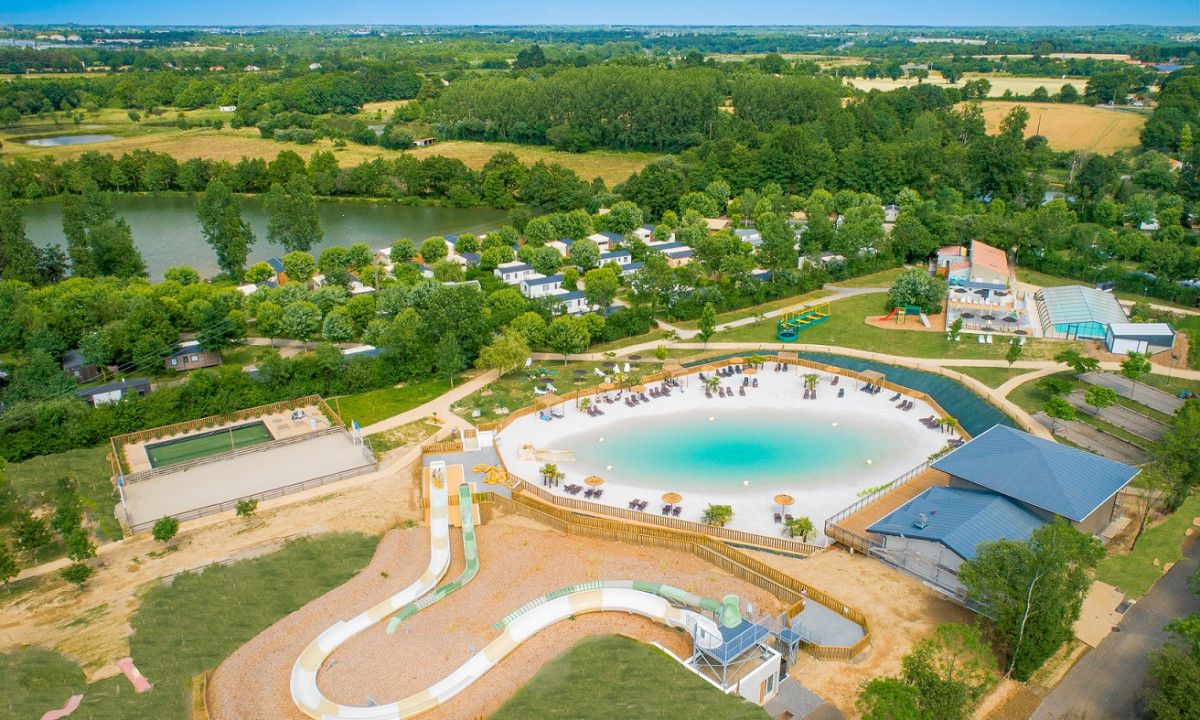A swimming pool with slides and loungers surrounded by greenery, buildings, and a lake at Campilo