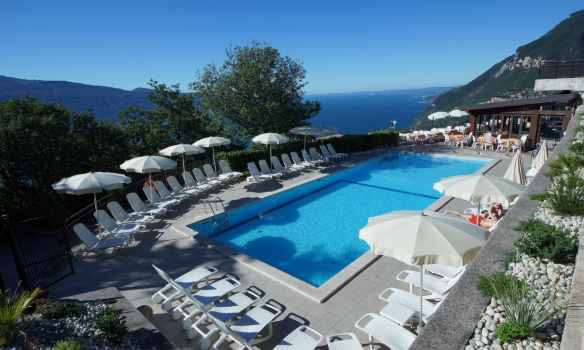 A large swimming pool surrounded by white loungers and umbrellas, overlooking mountainous landscape and a lake view at La Rotonda