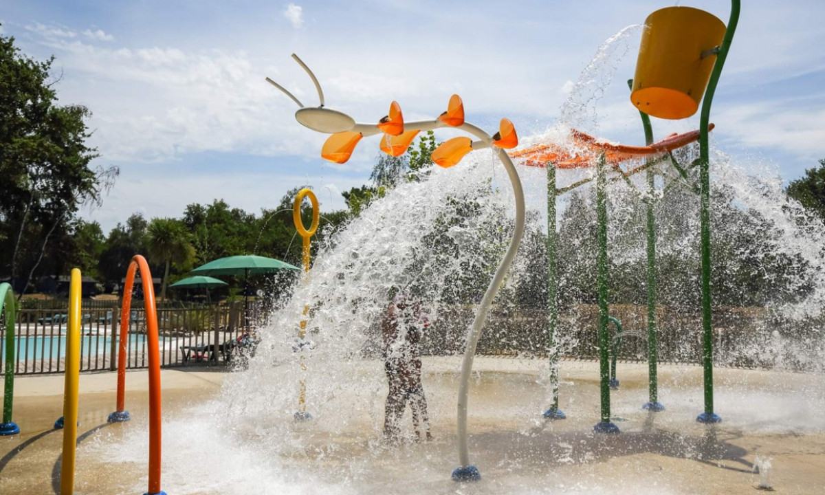 Water sprayers cascade over children playing on a splash pad surrounded by colorful equipment near a pool at Bordeaux Lac