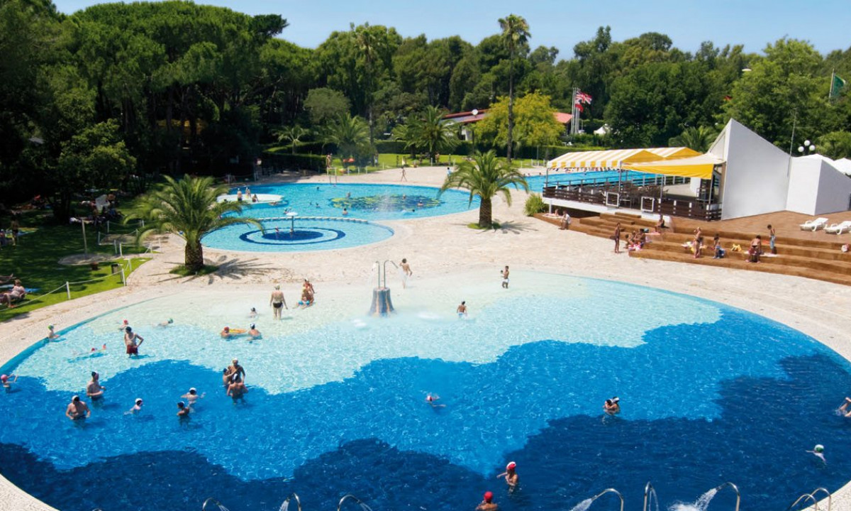 Circular pool with people swimming and lounging surrounded by trees and grassy area at Baia Domizia