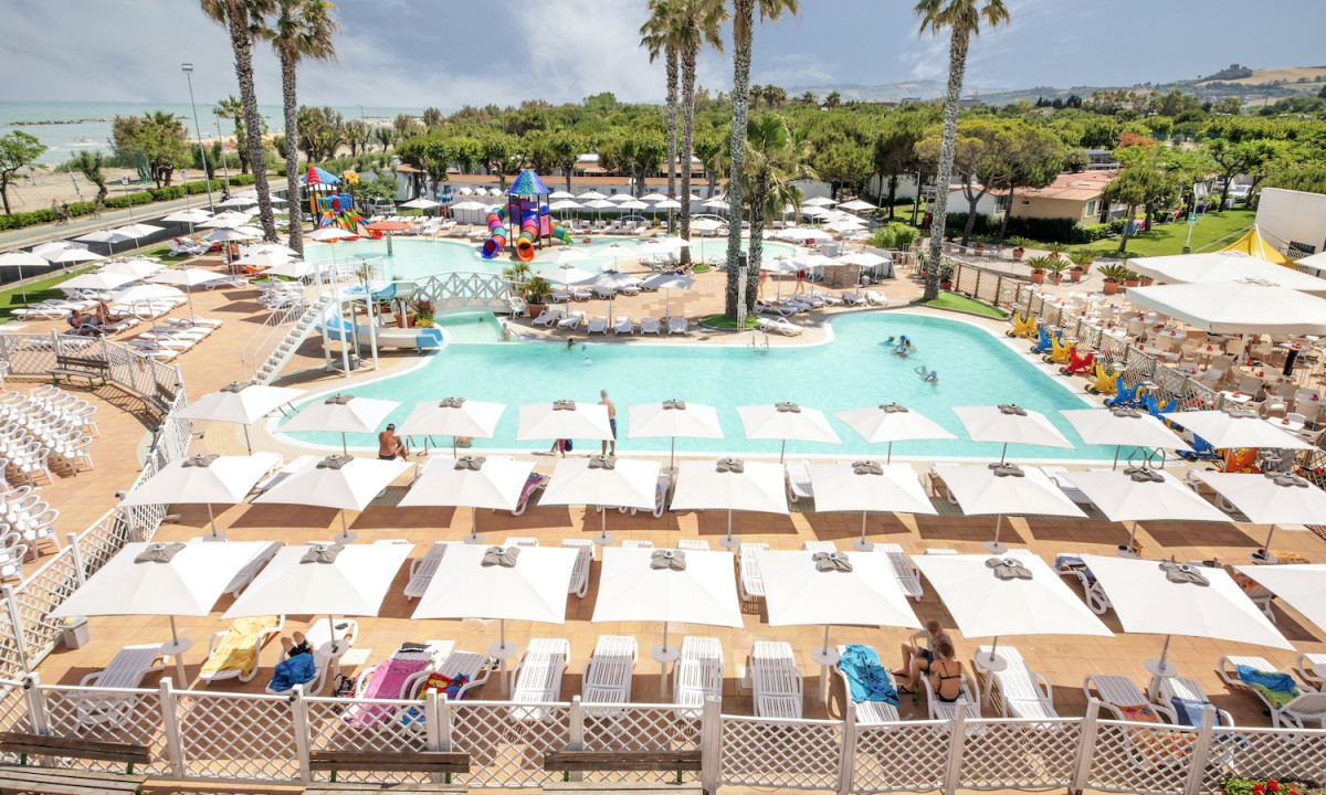 Pool with lounge chairs and umbrellas, children playing, set amidst palm trees and near a beach at Riva Nuova