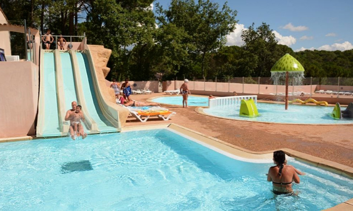 People sliding into a swimming pool, surrounded by trees and lounge chairs, under a clear sky at Lou Cantaire