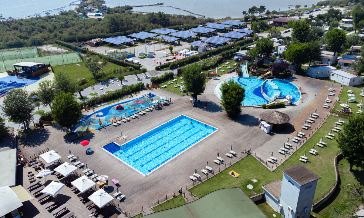 Swimming pools with lounge chairs and parasols, surrounded by trees and recreational areas near a waterfront at Spina Family Camping Village