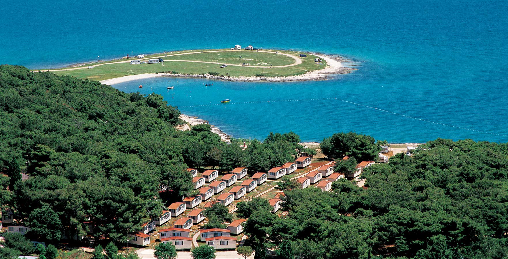 Cottages situated among dense trees, overlooking a small island surrounded by clear blue water at Stupice